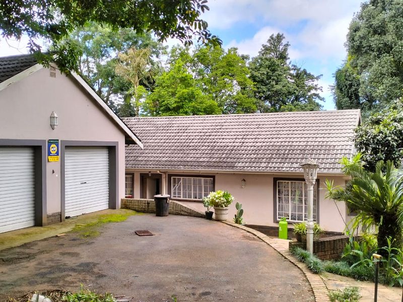 Front exterior view of the property featuring a double garage, asphalt driveway, and established garden surroundings.