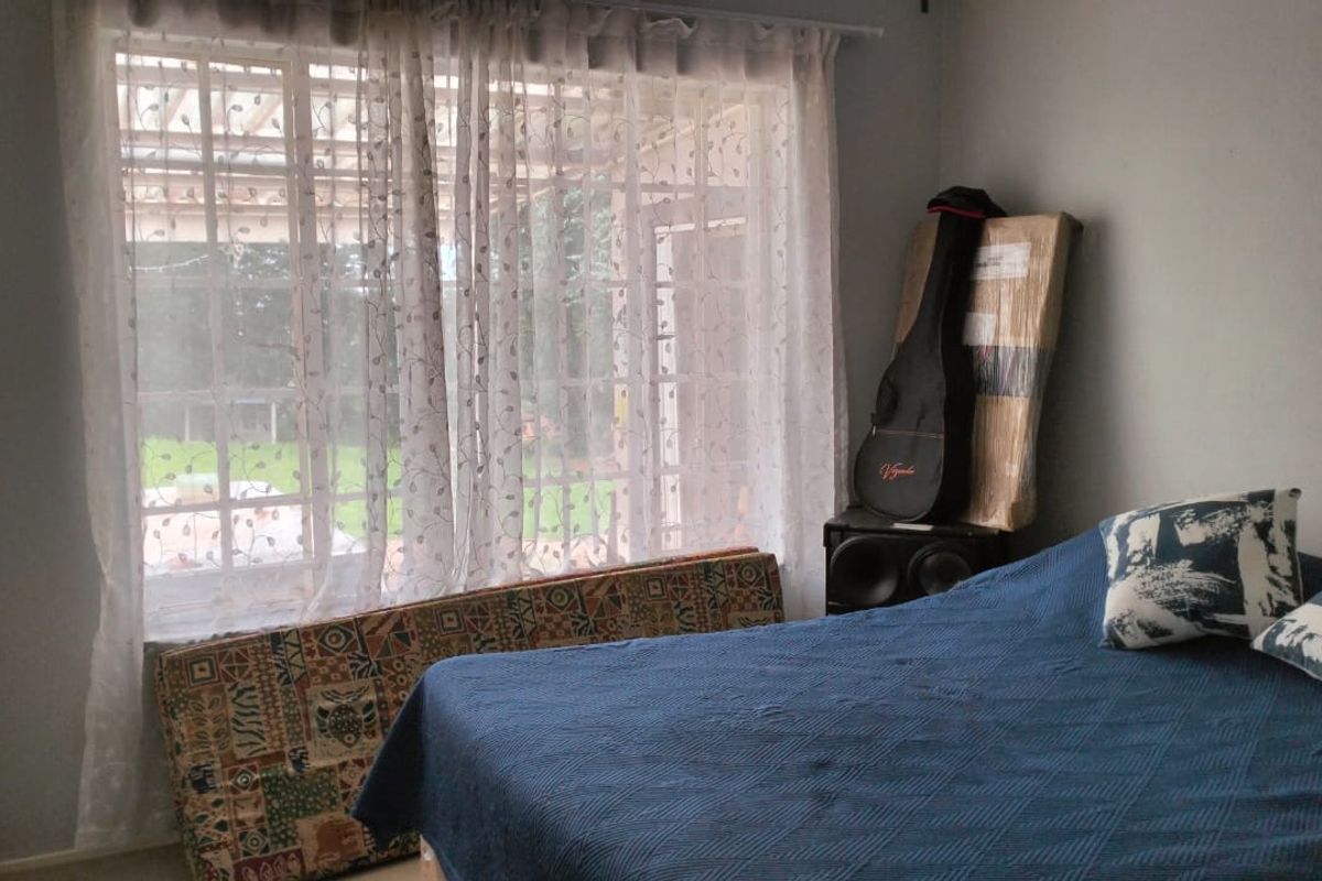 A bedroom featuring a large window with security bars, providing natural light and a view of the outdoor area.