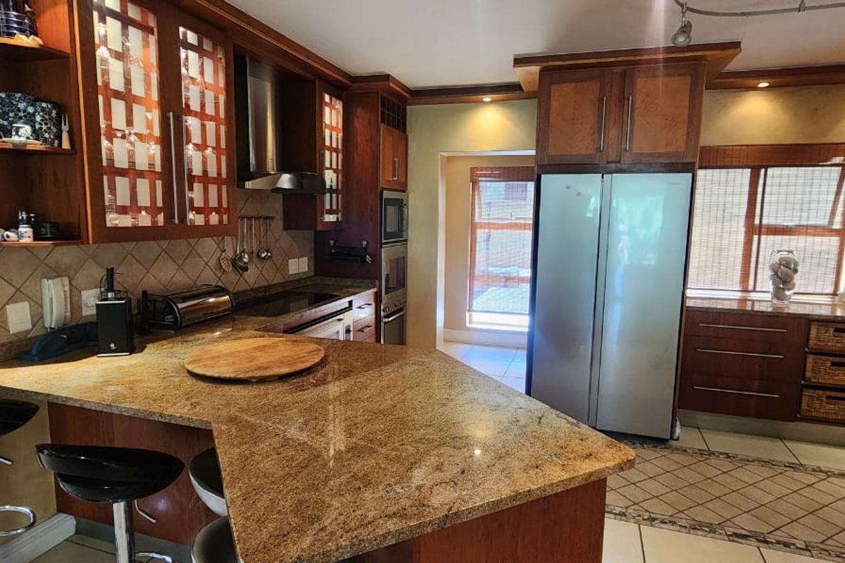 A functional kitchen featuring granite countertops, wooden cabinetry, built-in oven, extractor fan, and a breakfast bar area with tiled flooring.