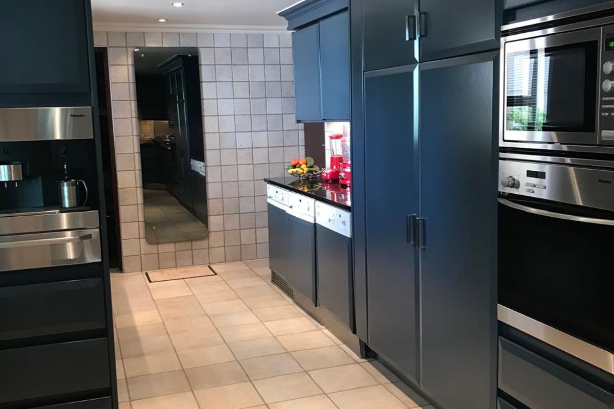 Modern kitchen featuring dark blue cabinetry, integrated Miele appliances, including a built-in coffee machine, oven, and microwave, with tiled flooring and recessed lighting.