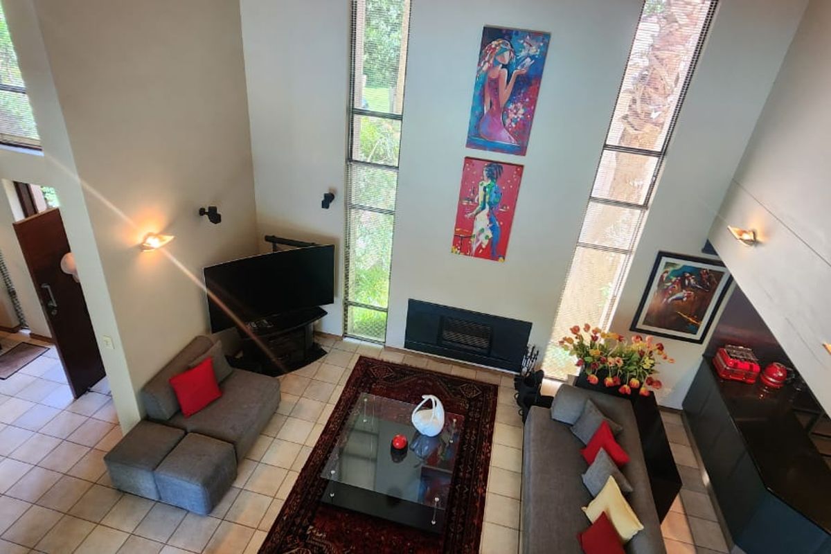 Spacious double-volume living area featuring a built-in fireplace, floor-to-ceiling windows, and tiled flooring, creating an airy and light-filled atmosphere.