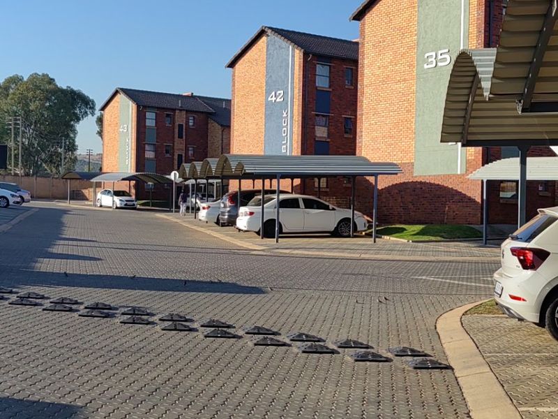 Exterior view of an apartment complex featuring brick buildings, paved parking areas, and covered carport structures.