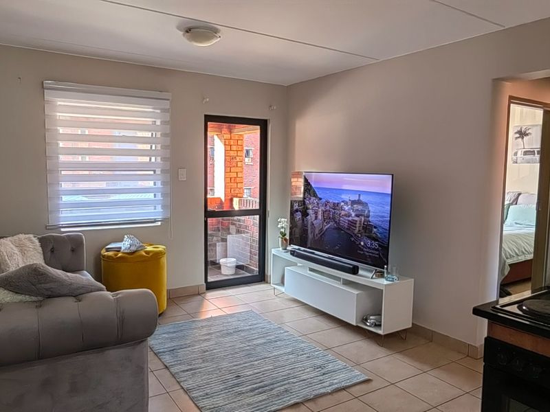 Open-plan living area featuring tiled flooring, a functional kitchen corner with built-in stove, and direct access to a private balcony.