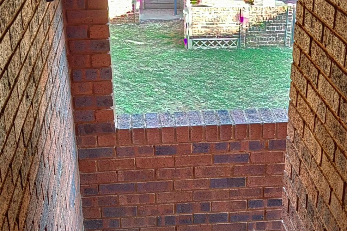 An exterior staircase featuring brick walls, slate tiling, and a metal handrail, leading down to a rear garden area.