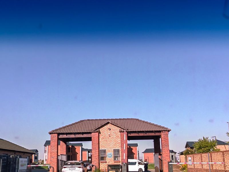 View of the apartment complex entrance featuring a brick security gatehouse, perimeter walling, and controlled access boom gates.