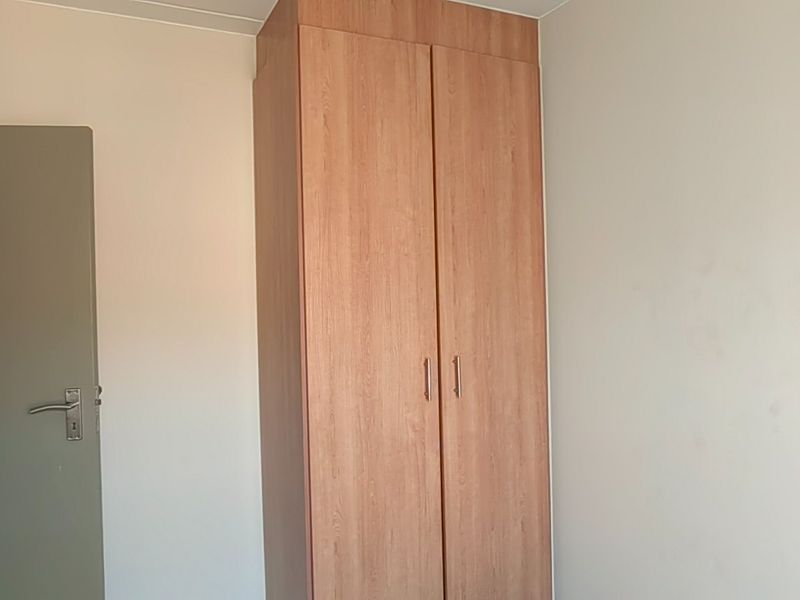 A simple bedroom featuring a built-in wooden wardrobe and neutral wall finishes.