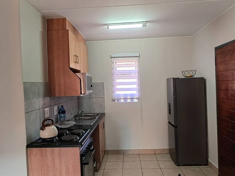 A functional kitchen featuring built-in wooden cabinetry, a hob, an oven, a stainless steel sink, and tiled flooring with a window for natural light.