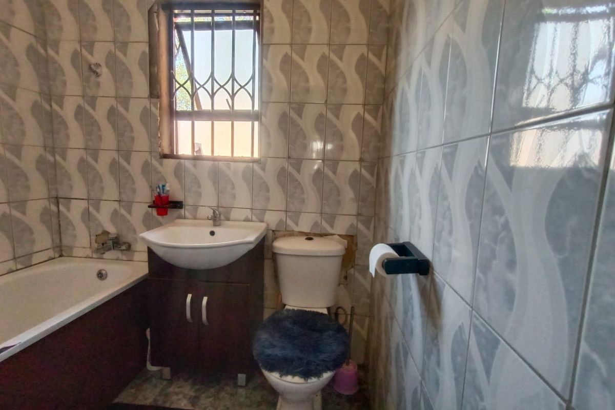 A compact bathroom featuring a bathtub, vanity basin, and toilet, finished with patterned wall tiles and a security-barred window.
