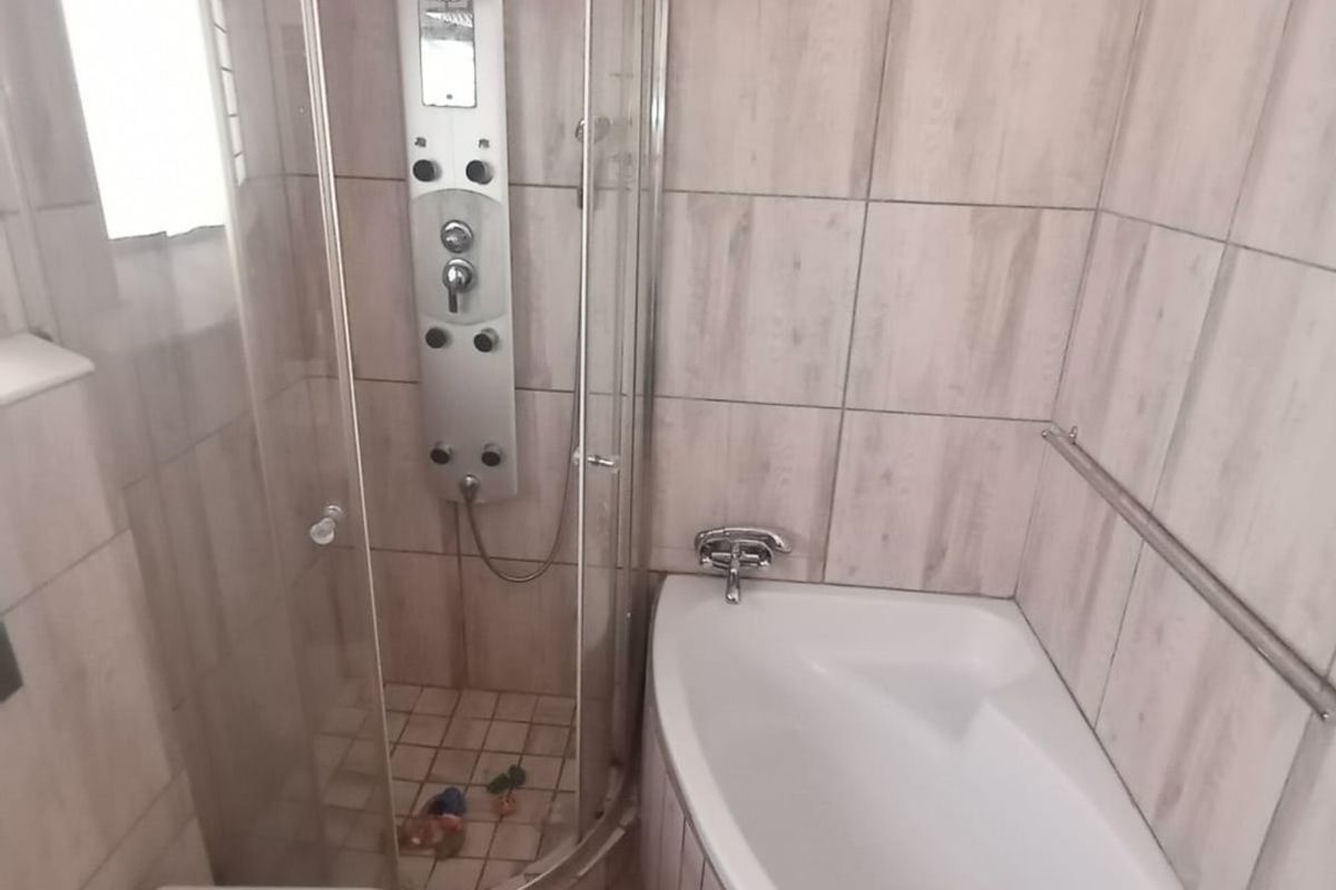 A modern bathroom featuring a corner bathtub, a separate glass-enclosed shower with a built-in shower panel, and a wall-mounted toilet.