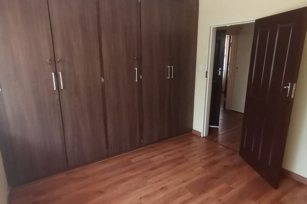 A bedroom featuring wood-look laminate flooring and a large, built-in dark wood wardrobe with ample storage space.