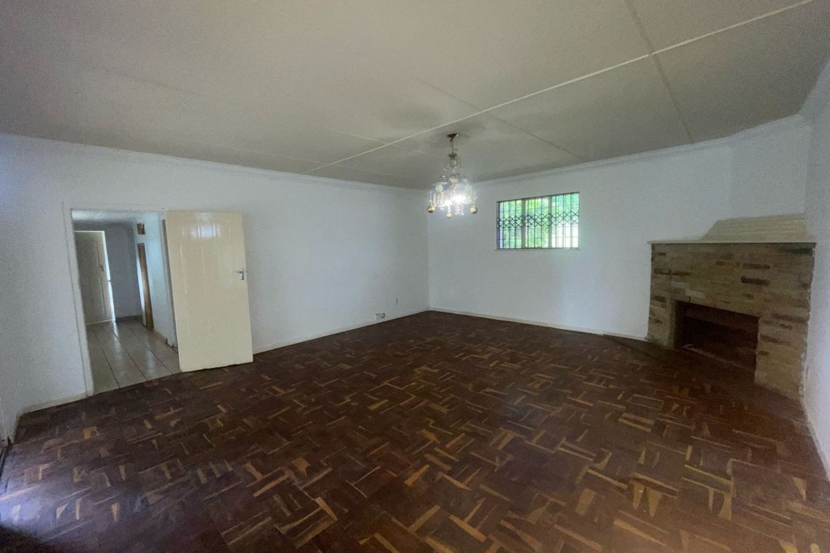 Spacious living room featuring original parquet flooring, a stone fireplace, and security bars on the window, offering a blank canvas for renovation.