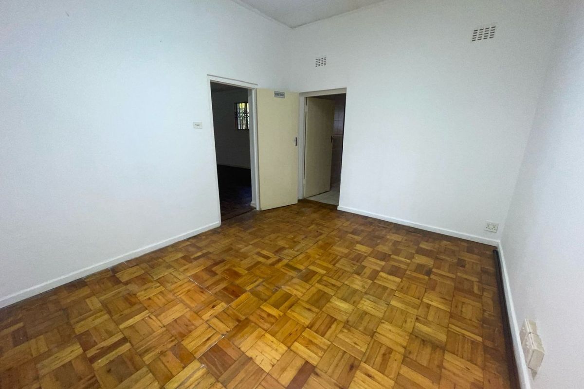 An empty bedroom featuring classic parquet flooring, neutral walls, and two doorways leading to adjacent rooms.