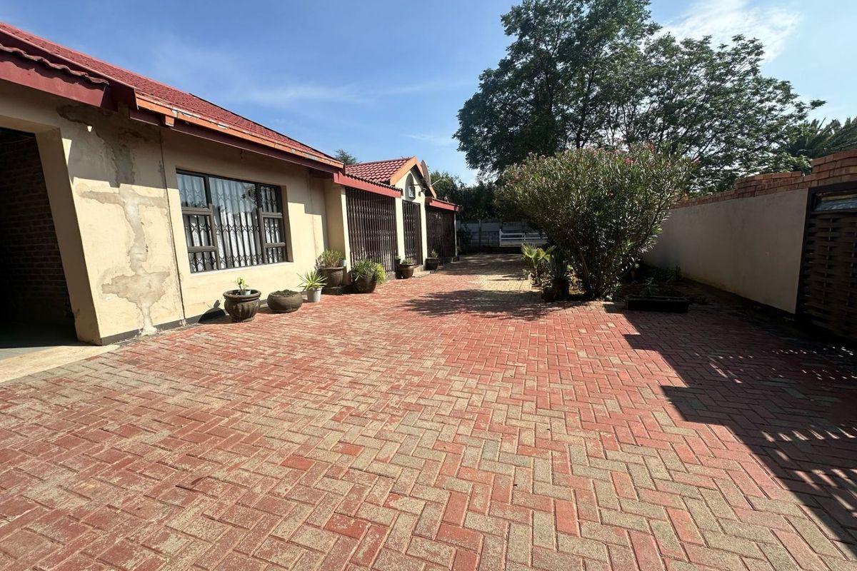 A paved rear courtyard area featuring a brick-built exterior wall with security bars on windows and a red tiled roof.