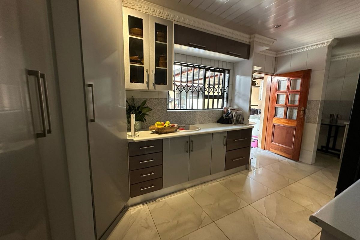 A functional kitchen featuring two-tone cabinetry, tiled flooring, a built-in sink, and a security gate on the window.
