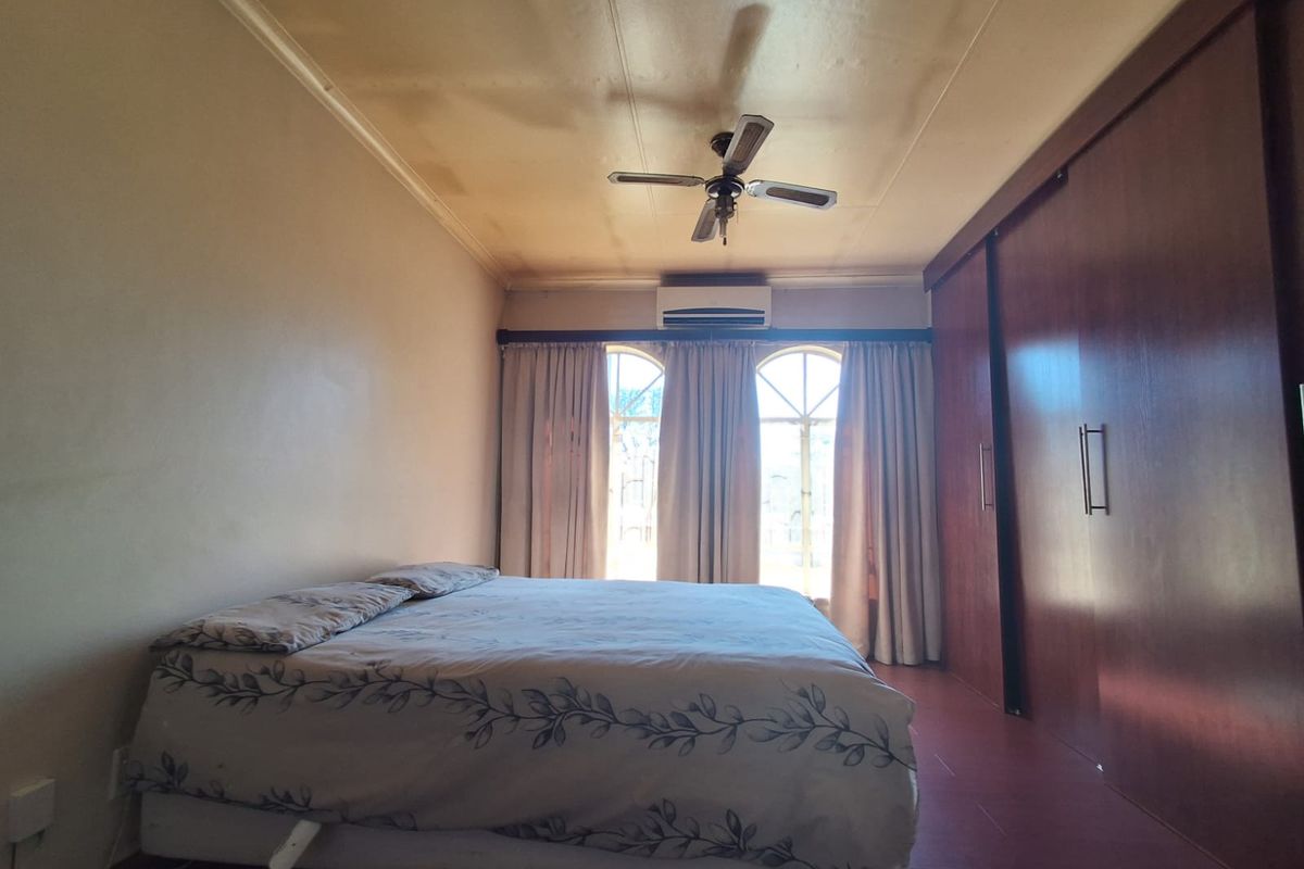 A bedroom featuring built-in wooden cupboards, a ceiling fan, and an air conditioning unit, with arched windows providing natural light.