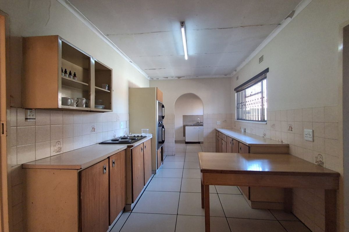 A dated kitchen featuring original wooden cabinetry, built-in oven and hob, tiled splashbacks, and tiled flooring, with an adjacent scullery area.