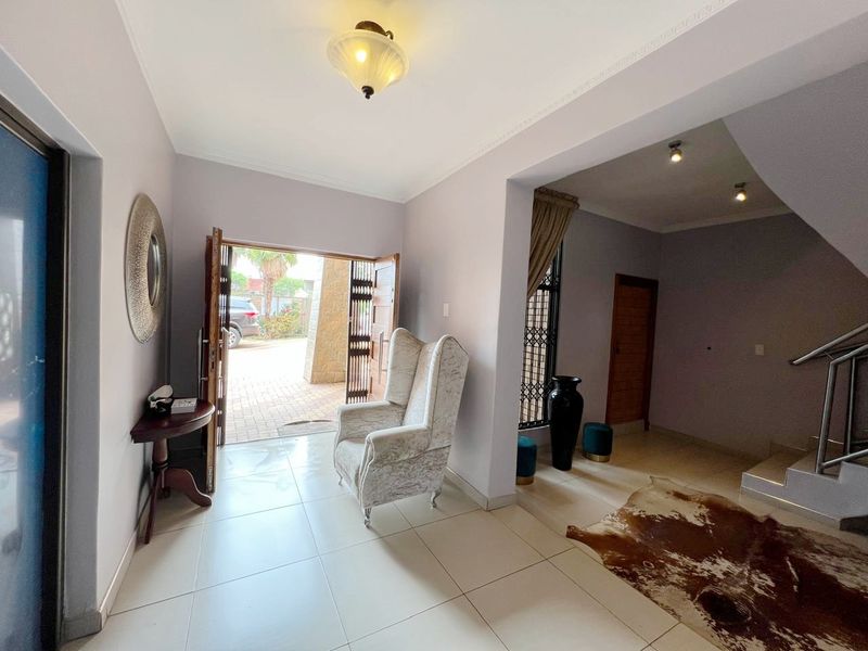 A bright and welcoming entrance hall featuring tiled flooring, decorative ceiling cornicing, and a staircase with a modern stainless steel handrail.