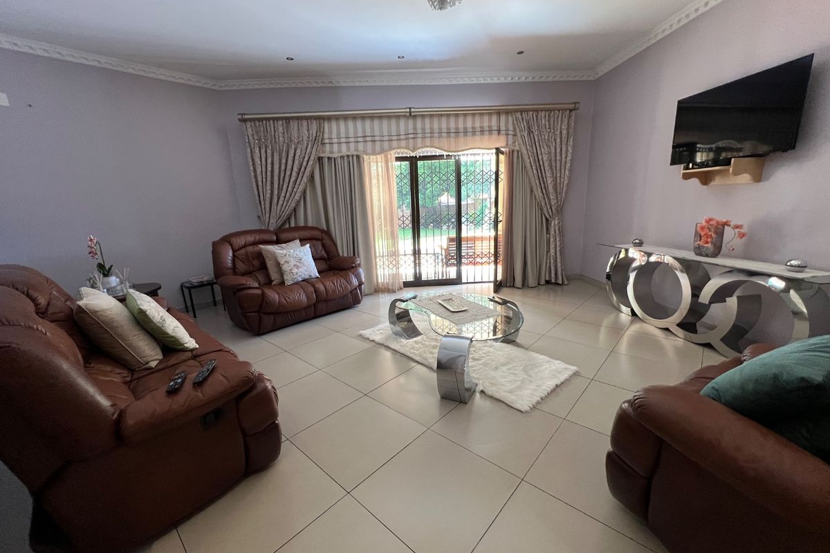 Spacious living room featuring large format floor tiles, decorative ceiling cornices, and sliding glass doors with security gates leading to the outdoor area.