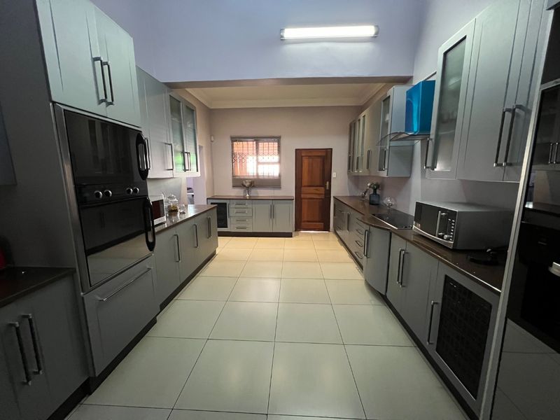 A spacious galley-style kitchen featuring modern grey cabinetry, dark countertops, built-in double ovens, and tiled flooring with ample storage space.