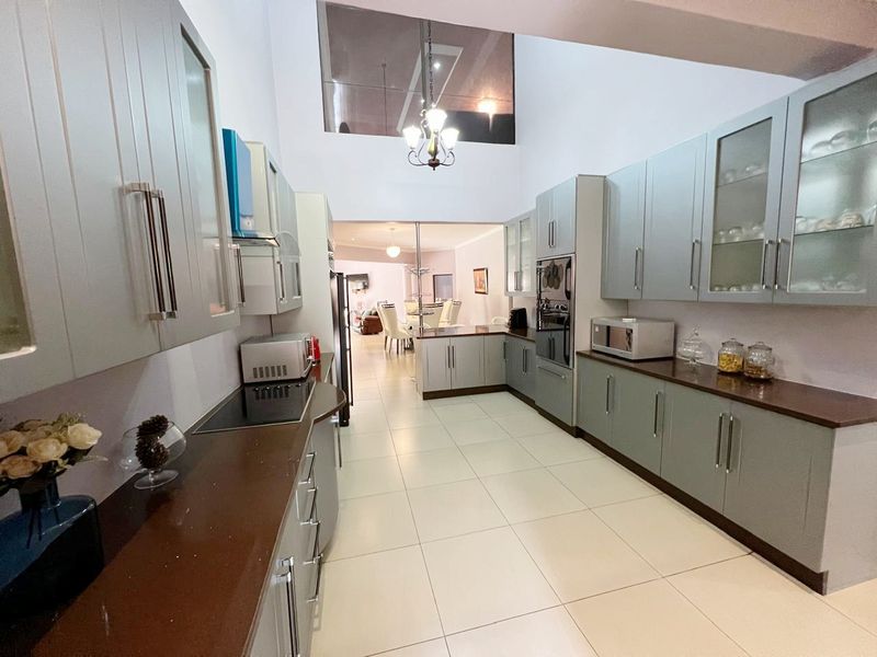 Spacious galley-style kitchen featuring light grey cabinetry, dark countertops, integrated oven, and a high-ceiling design leading into the dining area.