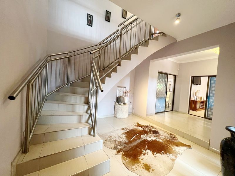 Spacious entrance hall featuring a tiled staircase with a modern stainless steel balustrade, leading to an open-plan living area.