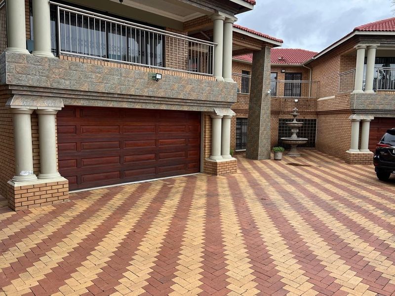A well-maintained exterior view of the property featuring a paved driveway, double garage, and decorative stone-clad pillars.