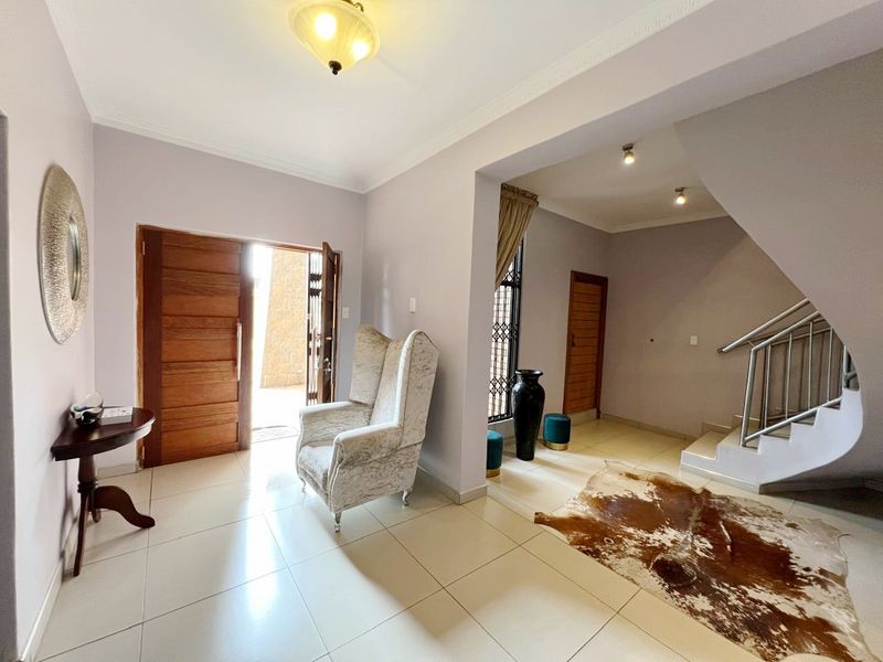 Spacious entrance hall featuring tiled flooring, a solid timber front door, and a staircase with a stainless steel balustrade.