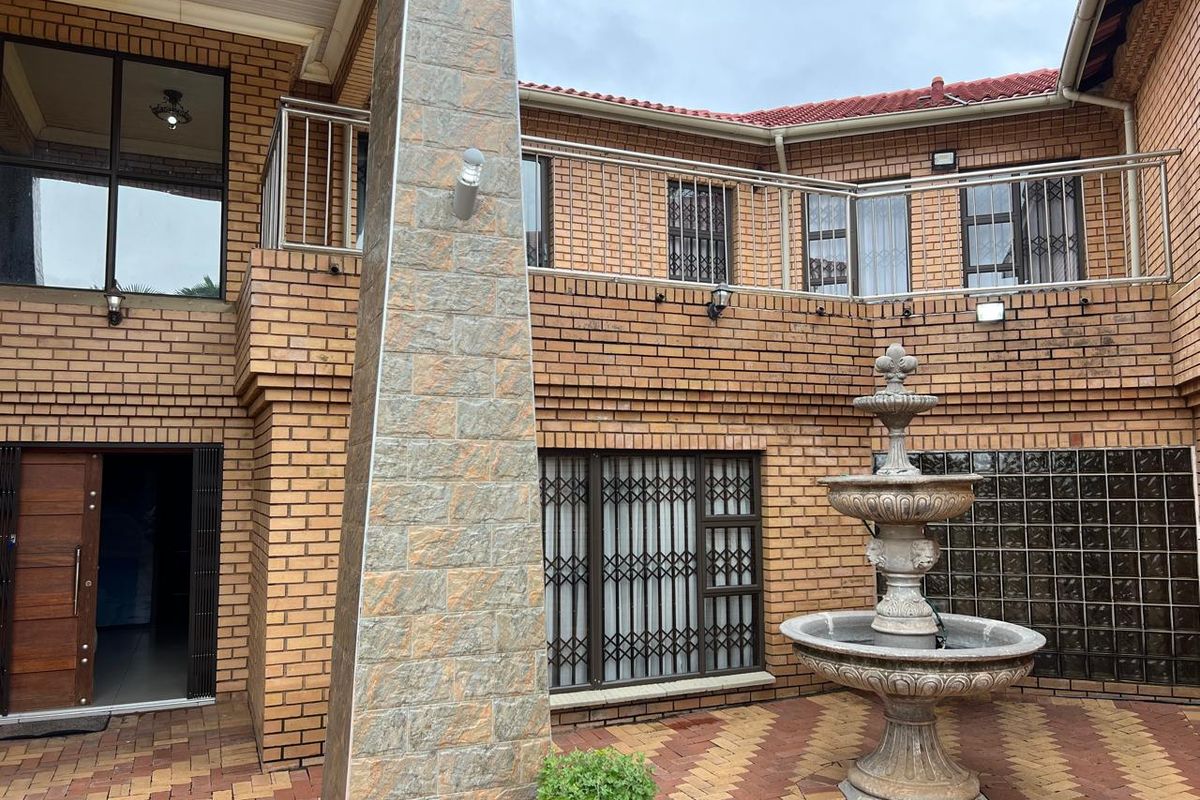A private courtyard featuring face-brick walls, a central stone fountain, paved flooring, and a balcony with stainless steel railings.