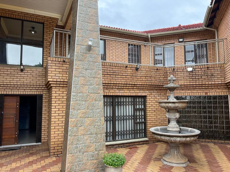 A private courtyard featuring face-brick walls, a central stone fountain, paved flooring, and a balcony with stainless steel railings.