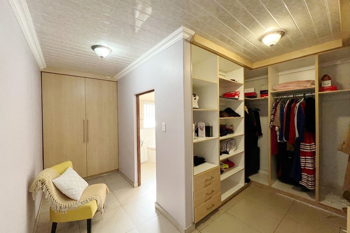 A walk-in closet featuring built-in cabinetry, open shelving, and tiled flooring, with direct access to an adjoining bathroom.