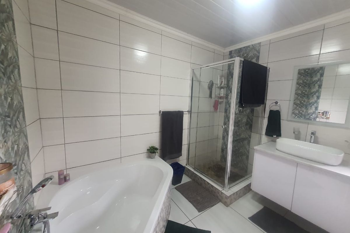 A modern bathroom featuring a corner bathtub, a glass-enclosed shower, and a wall-mounted vanity with a vessel sink.