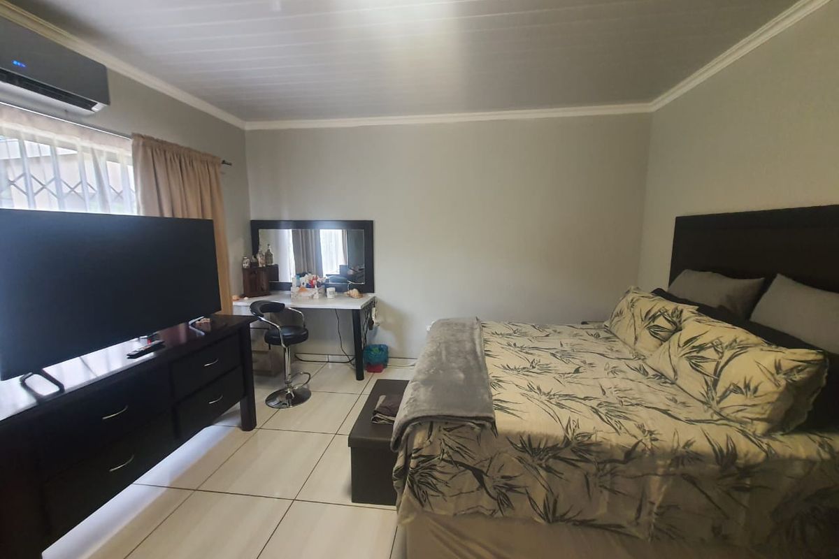 A bedroom featuring tiled flooring, a wall-mounted air conditioning unit, and security bars on the window.