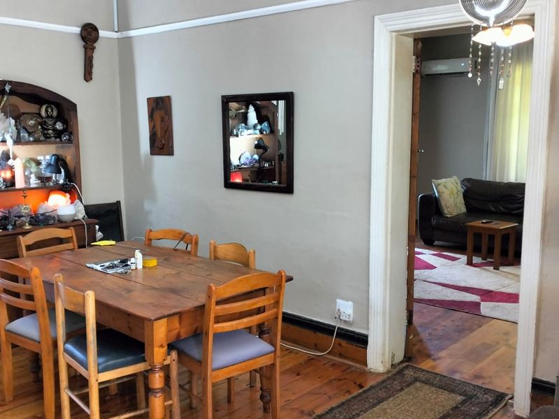 A dining room featuring polished hardwood flooring and traditional skirting boards, with an open doorway leading into an adjacent living area.