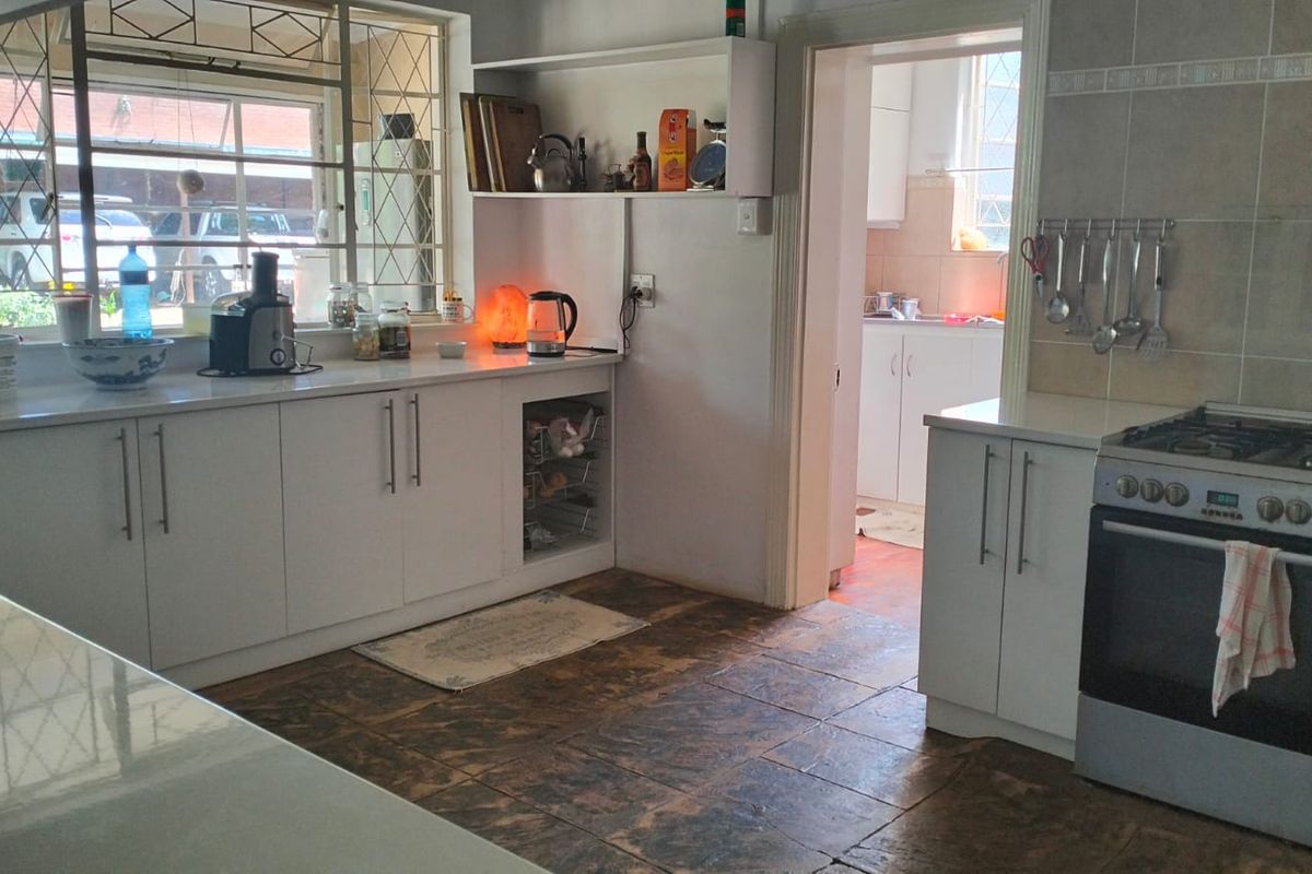 A functional kitchen featuring white cabinetry, stone countertops, a gas stove, and a tiled backsplash, with an adjacent scullery area visible through the doorway.
