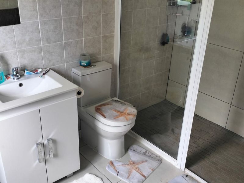 A functional bathroom featuring a vanity cabinet with basin, a standard toilet, and a glass-enclosed shower with tiled finishes.