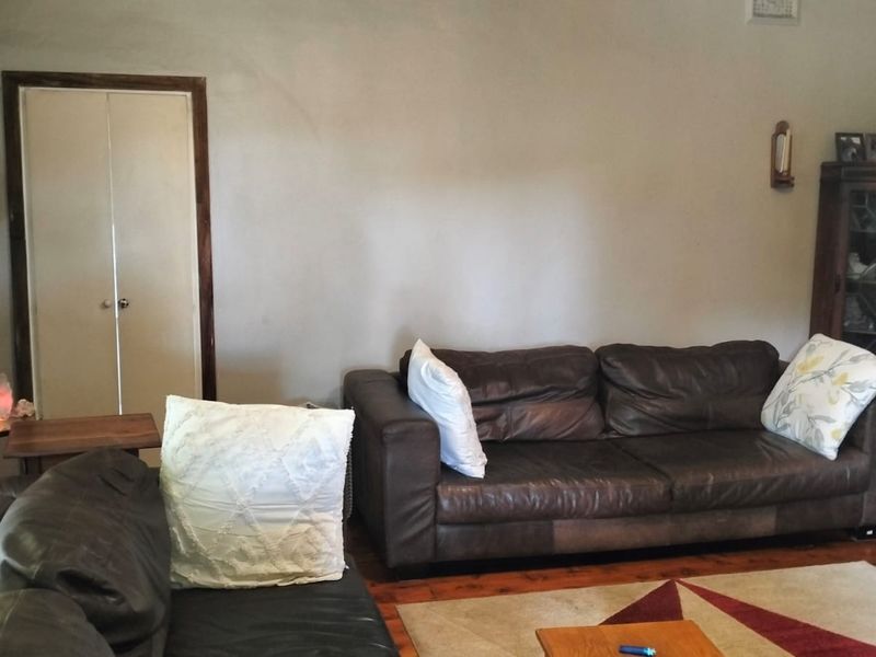 A living room featuring hardwood flooring and a built-in cupboard, showing signs of wear including visible wall cracks.