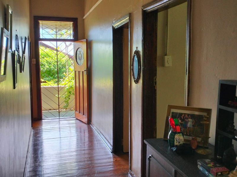 A traditional hallway featuring polished hardwood flooring and timber door frames, leading to an exterior door with a decorative security gate.