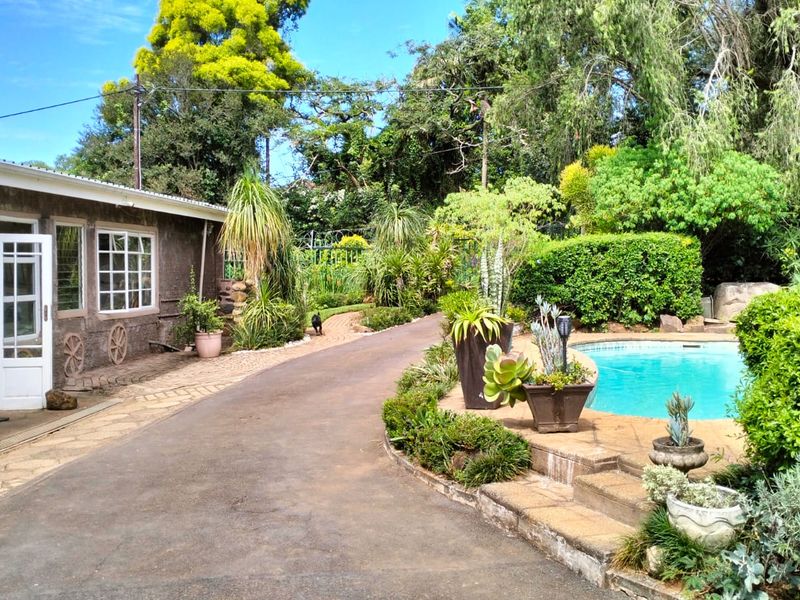 A lush rear garden area featuring a swimming pool, paved pathways, and direct access to the home through classic french doors.