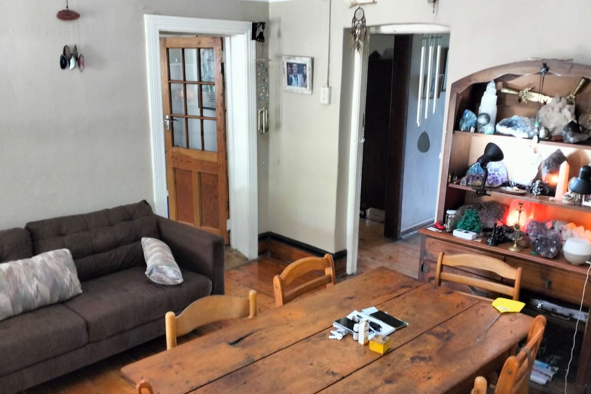 A living area featuring timber flooring, a classic timber door with glass panes, and an open archway leading to adjacent rooms.