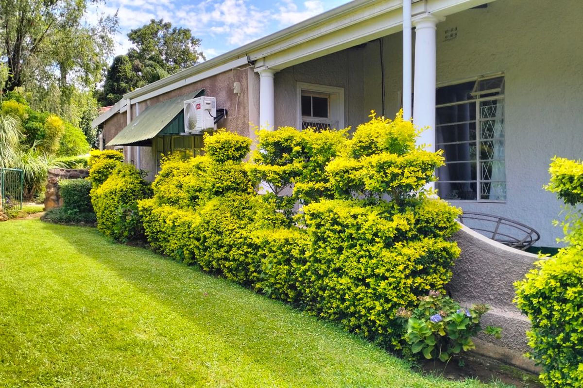 A view of the rear exterior featuring a covered patio area, established garden landscaping, and an external air conditioning unit mounted on the wall.