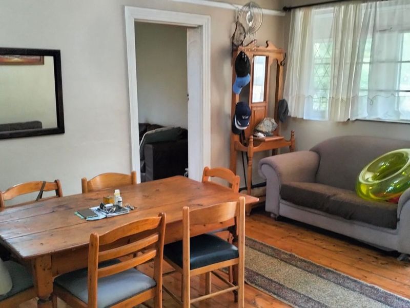 A dining room featuring original hardwood flooring and neutral wall finishes, providing a functional space with direct access to the adjacent living area.