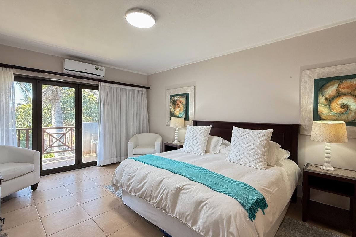 A well-maintained bedroom featuring tiled flooring, a wall-mounted air conditioning unit, and sliding glass doors providing access to a private balcony.