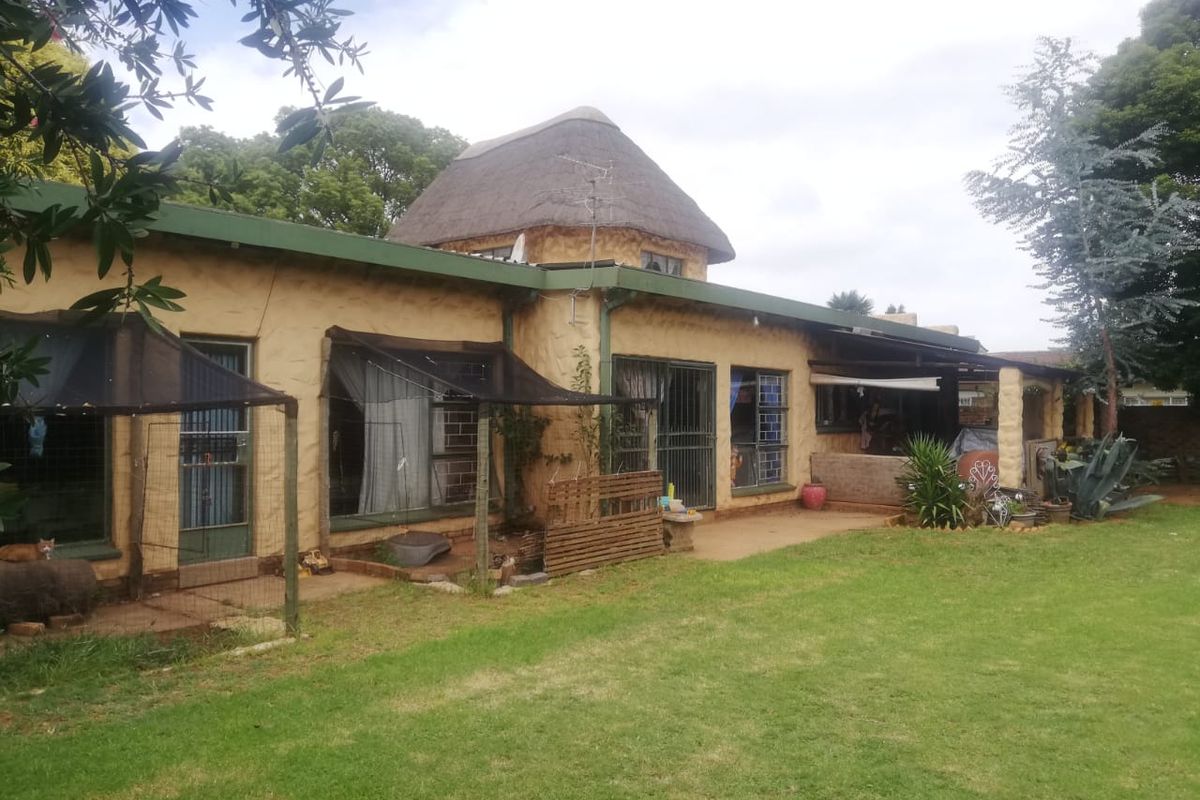 Rear view of a single-story house featuring a thatched roof, textured exterior walls, and a covered patio area overlooking a spacious garden.