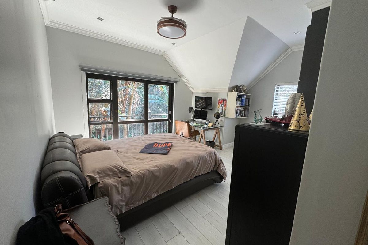 A spacious bedroom featuring a sloped ceiling, recessed lighting, a ceiling fan, and large windows that provide natural light and garden views.