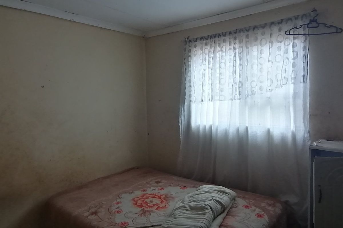 A bedroom featuring plain walls and a window with curtains, requiring cosmetic updates and wall refinishing to improve the overall condition.