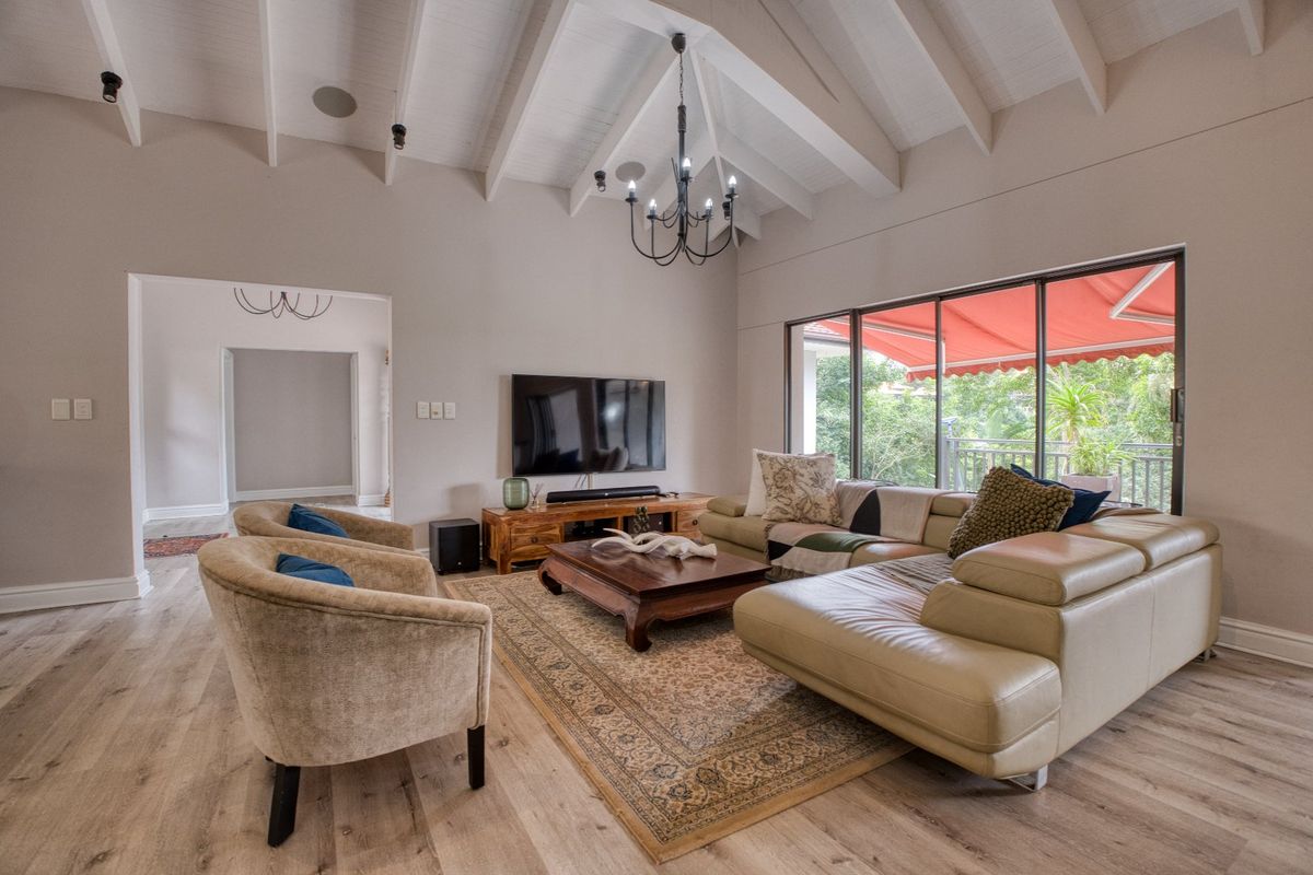 Spacious living room featuring high vaulted ceilings with exposed beams, large sliding glass doors leading to a balcony, and modern wood-look flooring.