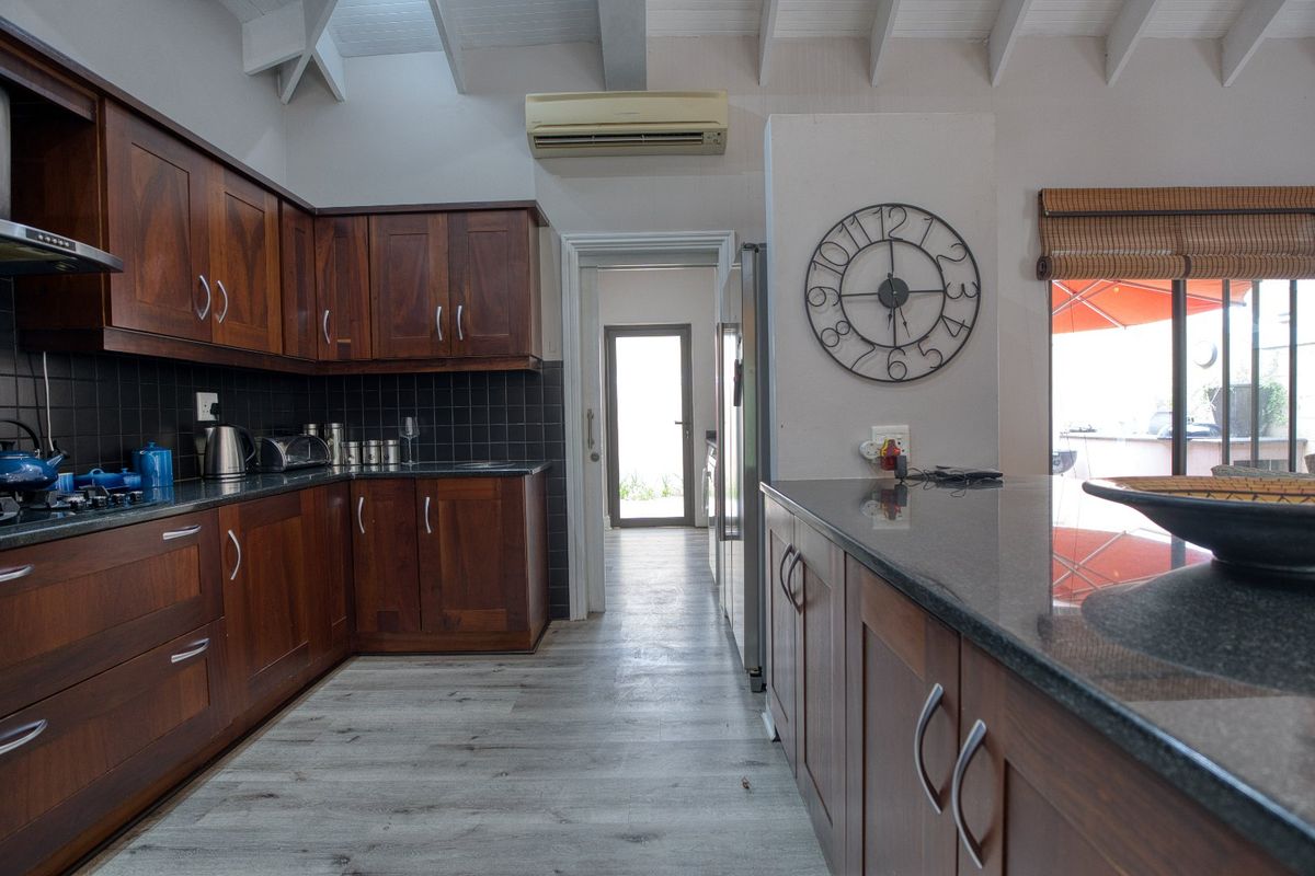 A functional kitchen featuring dark wood cabinetry, granite countertops, black tiled backsplash, and vaulted ceilings with exposed beams.