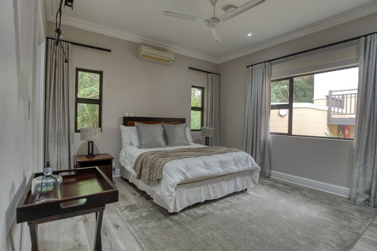 A well-maintained bedroom featuring neutral wall tones, tiled flooring, a ceiling fan, and a wall-mounted air conditioning unit.