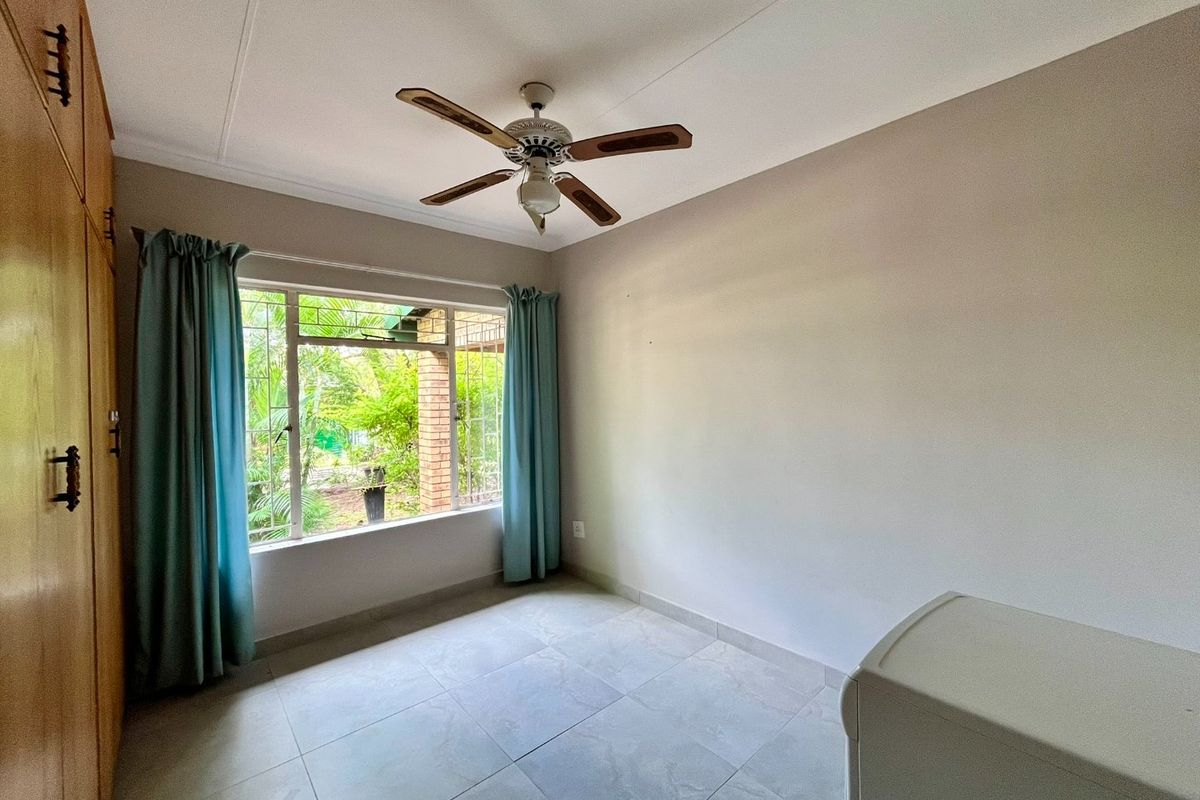 A bright bedroom featuring large windows, tiled flooring, a ceiling fan, and built-in wooden cupboards.