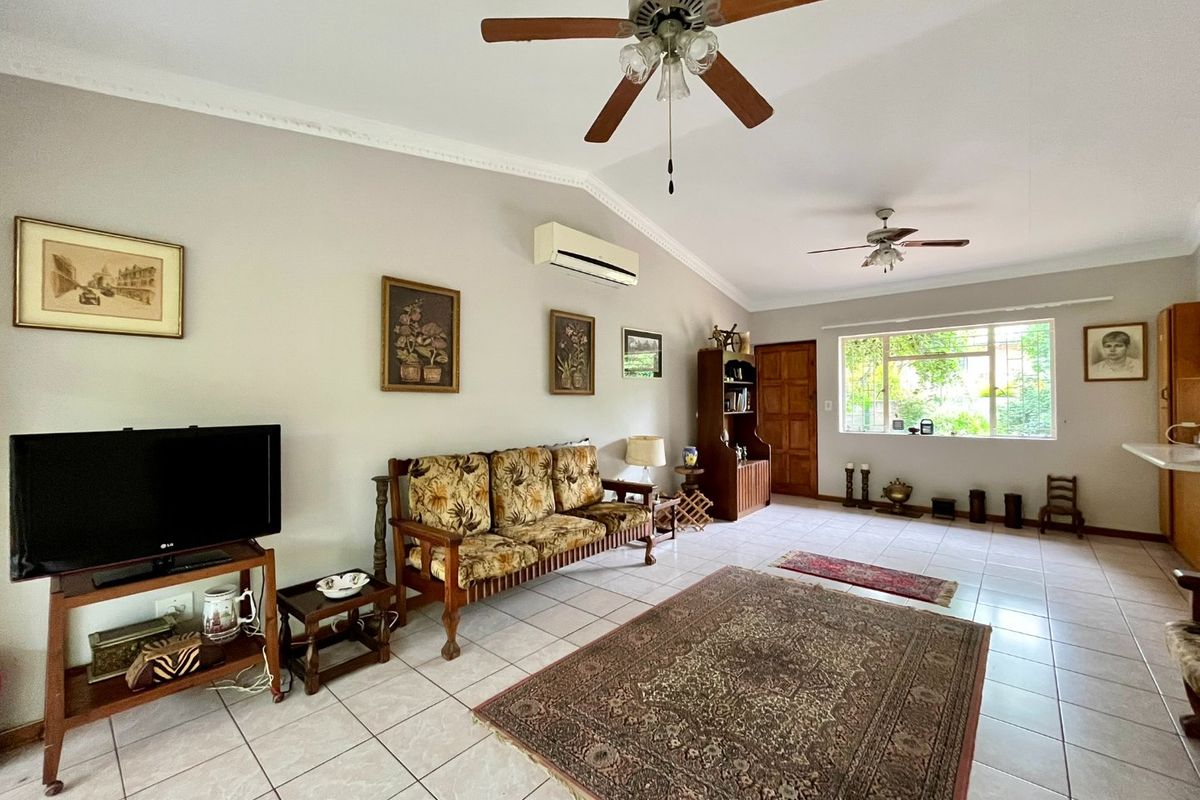 Spacious living room featuring tiled flooring, dual ceiling fans, and a wall-mounted air conditioning unit, offering a comfortable and functional living space.